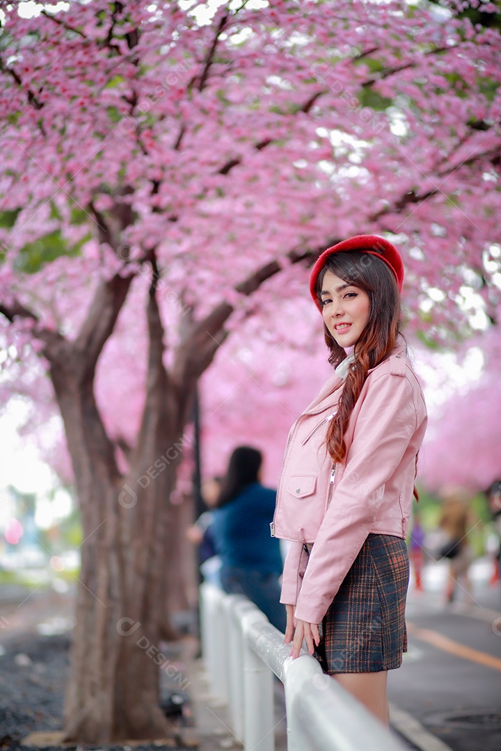 Uma mulher viajante hipster passear usa um chapéu vermelho e um vestido de couro liso com uma bela árvore de flores de cerejeira sakura desabrochando na cor rosa no parque em um dia de primavera.