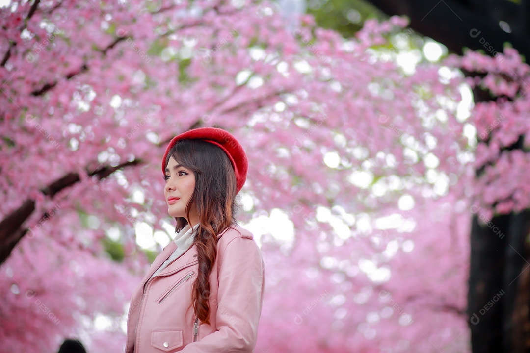 Uma mulher viajante hipster passear usa um chapéu vermelho e um vestido de couro liso com uma bela árvore de flores de cerejeira sakura desabrochando na cor rosa no parque em um dia de primavera.