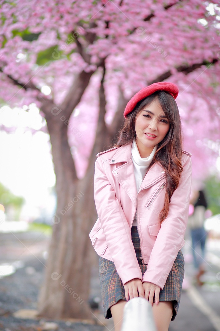 Uma mulher viajante hipster passear usa um chapéu vermelho e um vestido de couro liso com uma bela árvore de flores de cerejeira sakura desabrochando na cor rosa no parque em um dia de primavera.