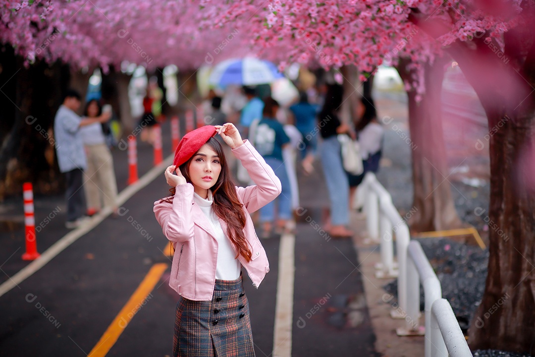 Uma mulher viajante hipster passear usa um chapéu vermelho e um vestido de couro liso com uma bela árvore de flores de cerejeira sakura desabrochando na cor rosa no parque em um dia de primavera.