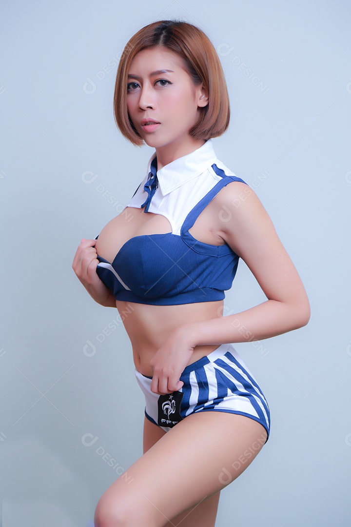 Linda e sexy líder de torcida posando de mulher vestida com roupas esportivas, jogando futebol em fundo branco.