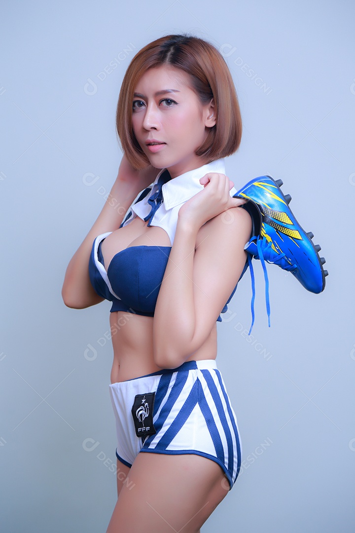 Linda e sexy líder de torcida posando de mulher vestida com roupas esportivas, jogando futebol em fundo branco.