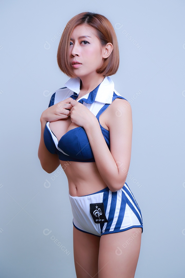 Linda e sexy líder de torcida posando de mulher vestida com roupas esportivas, jogando futebol em fundo branco.