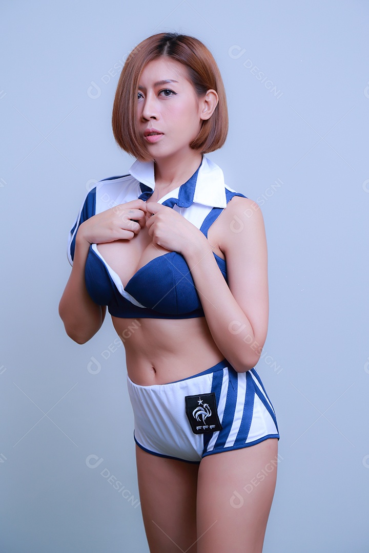 Linda e sexy líder de torcida posando de mulher vestida com roupas esportivas, jogando futebol em fundo branco.