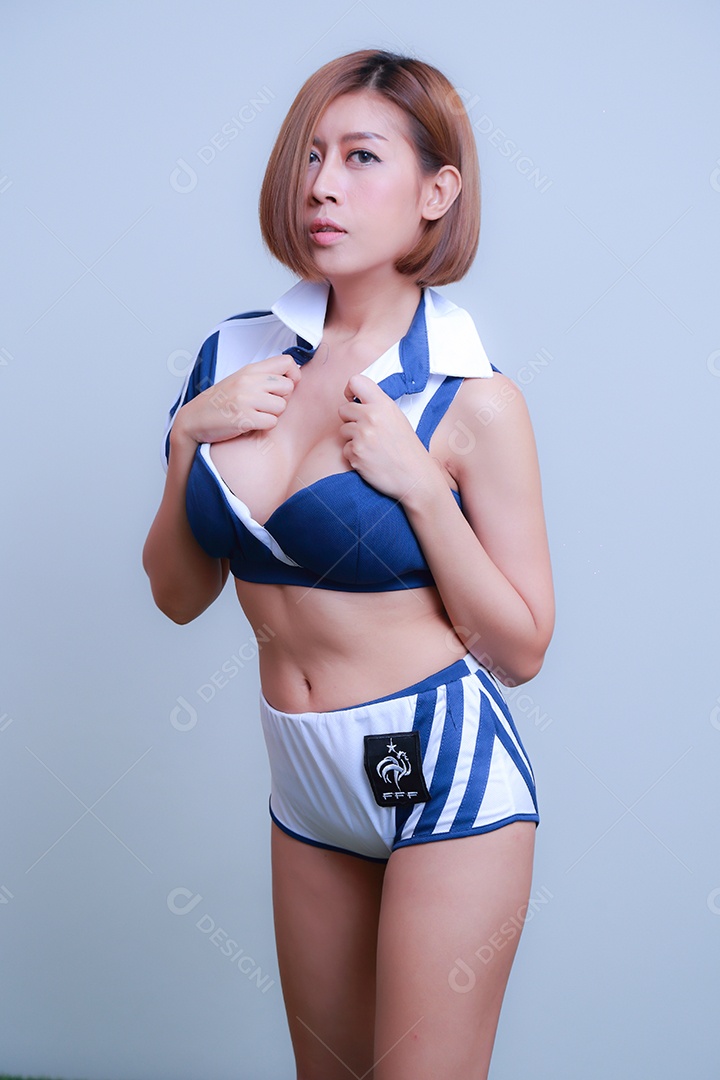 Linda e sexy líder de torcida posando de mulher vestida com roupas esportivas, jogando futebol em fundo branco.