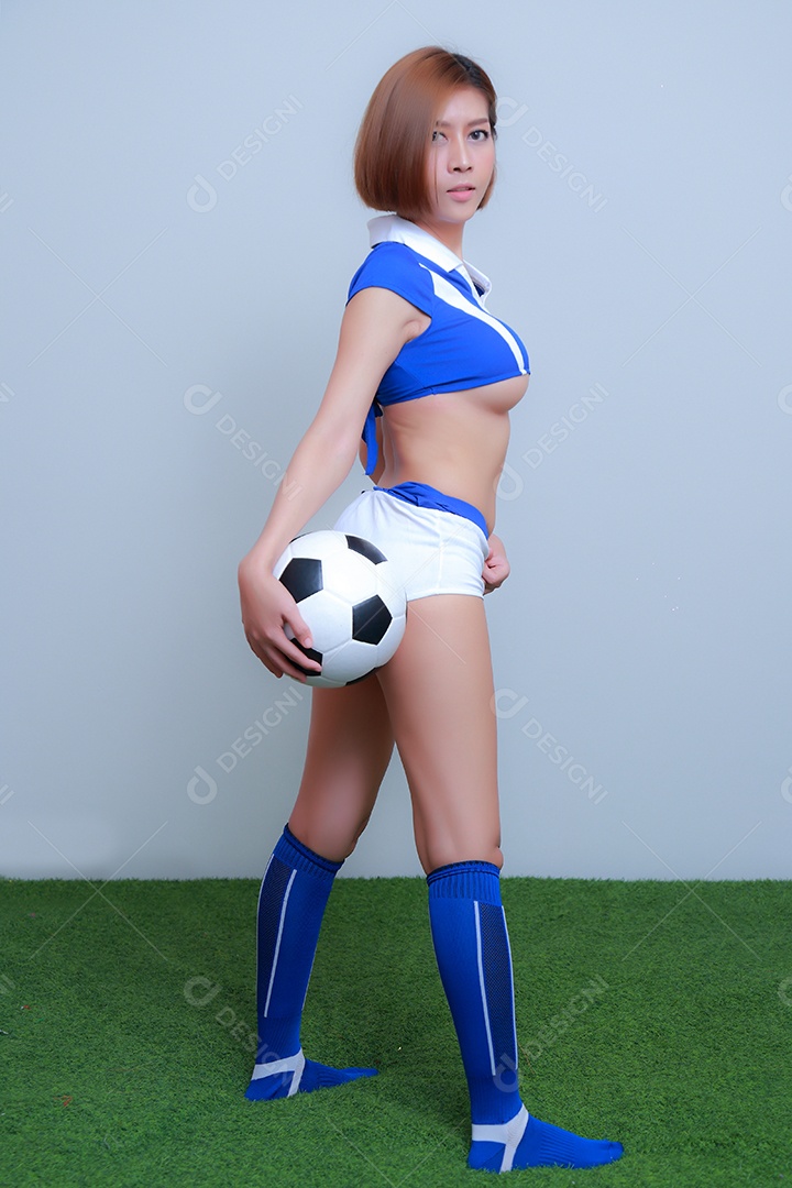 Linda e sexy líder de torcida posando de mulher vestida com roupas esportivas, jogando futebol em fundo branco.