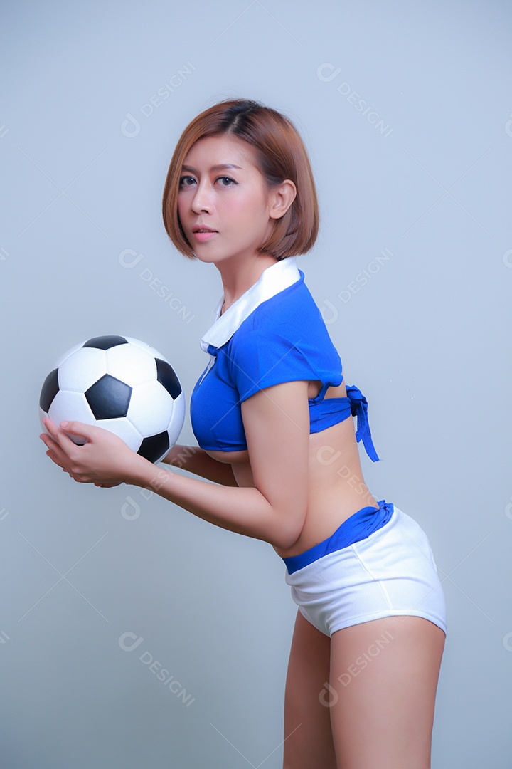 Linda e sexy líder de torcida posando de mulher vestida com roupas esportivas, jogando futebol em fundo branco.