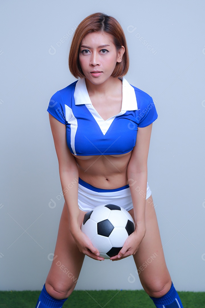 Linda e sexy líder de torcida posando de mulher vestida com roupas esportivas, jogando futebol em fundo branco.