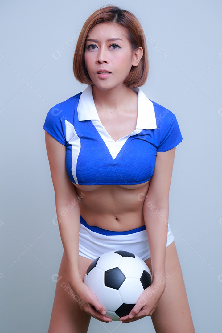 Linda e sexy líder de torcida posando de mulher vestida com roupas esportivas, jogando futebol em fundo branco.