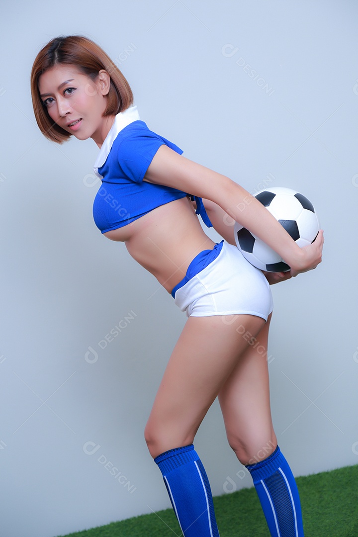 Linda e sexy líder de torcida posando de mulher vestida com roupas esportivas, jogando futebol em fundo branco.