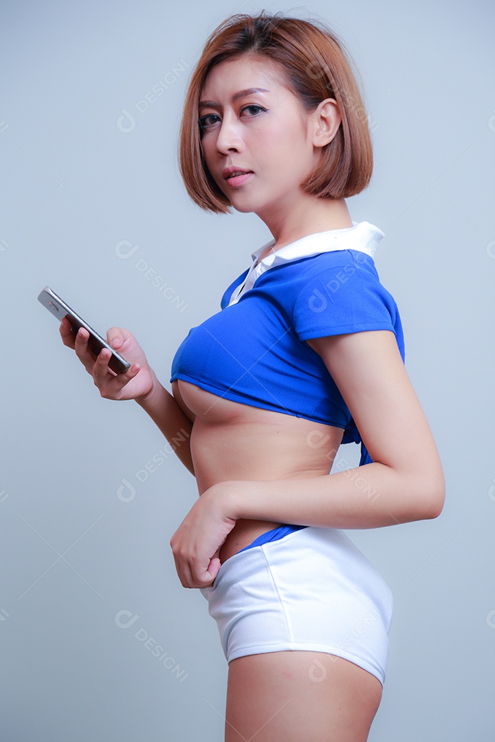 Linda e sexy líder de torcida posando de mulher vestida com roupas esportivas, jogando futebol em fundo branco.