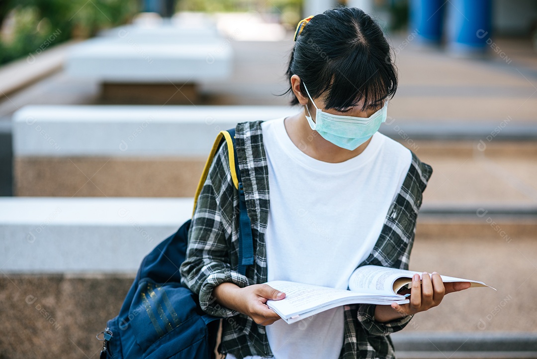 Estudantes do sexo feminino usam máscaras, ficam nas escadas e seguram livros.