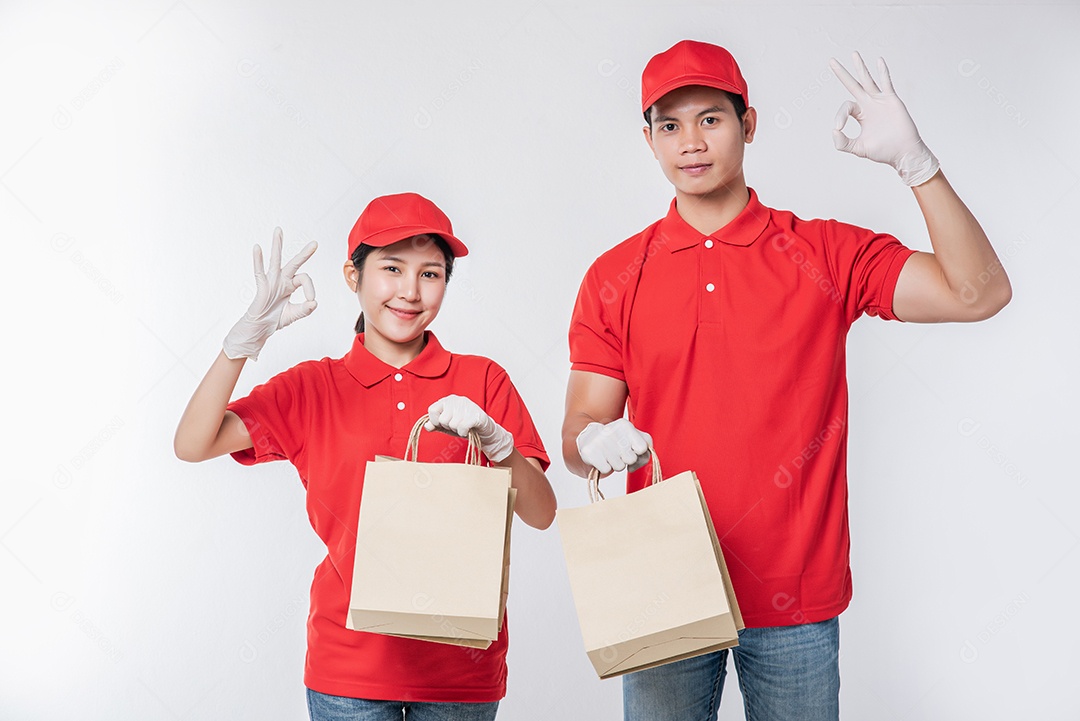 Imagem de um jovem entregador feliz em uniforme de camiseta em branco de boné vermelho em pé com pacote de papel ofício marrom vazio isolado