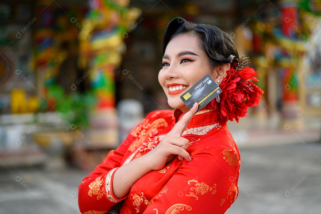 Retrato de uma linda mulher asiática usando um cheongsam sorrindo e poses mostram cartão de crédito no santuário no Ano Novo Chinês