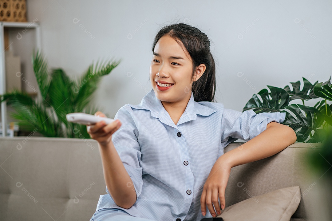Smiley jovem segurando e usar o controle remoto para abrir o ar condicionado na sala de estar em casa