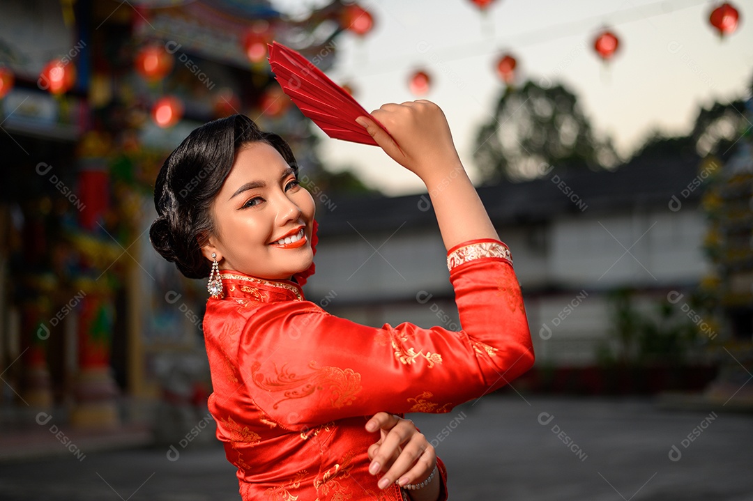 Retrato de uma linda mulher asiática vestindo um cheongsam sorrindo e segurando envelopes vermelhos em pose de fã no santuário no Ano Novo Chinês