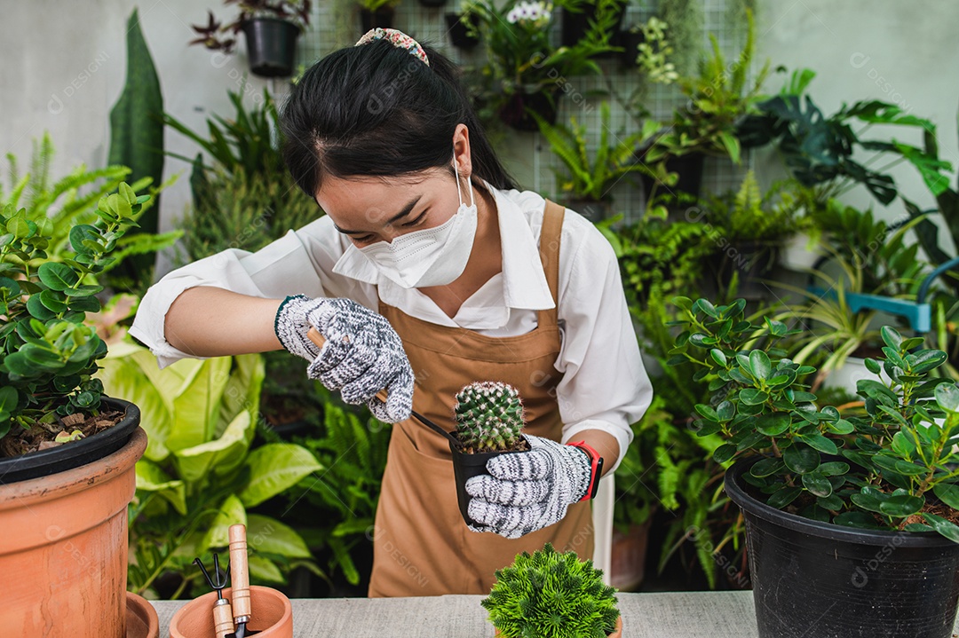 Mulher jardineira asiática usando máscara facial e suporte de avental e mostrando uma pá e forcado, equipamento para transplantes de plantas de interior