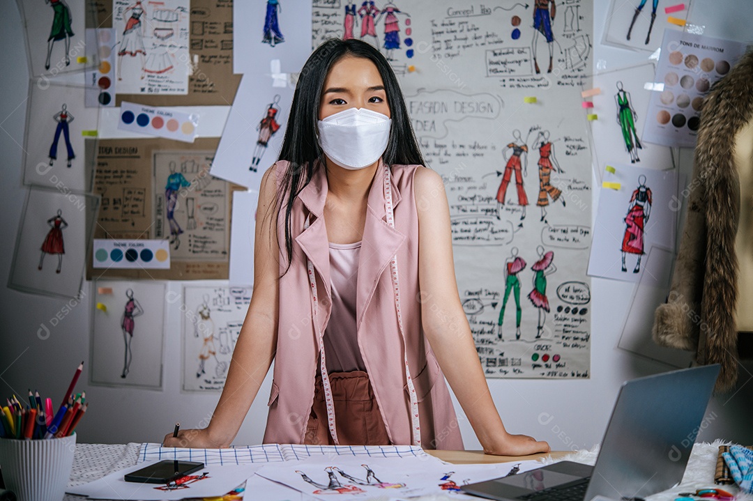 Retrato feminino asiático jovem permanente no atelier moderno. Trabalhadora criativa de mulher positiva usando máscara facial médica em estúdio. distância e novo conceito normal