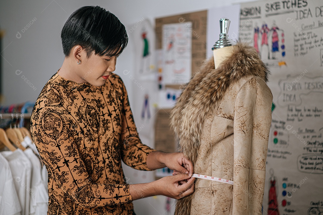 Retrato de um jovem alfaiate asiático medindo a cintura do manequim na mesa no estúdio de moda. Designer e conceito LGBTQ.