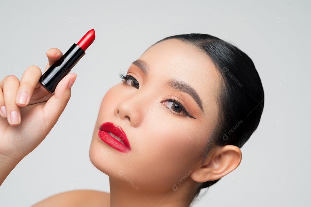 Retrato de mulher asiática bonita com batom na mão. O cabelo saudável e a pele dos cuidados com a pele fecham a beleza do rosto isolada sobre o fundo