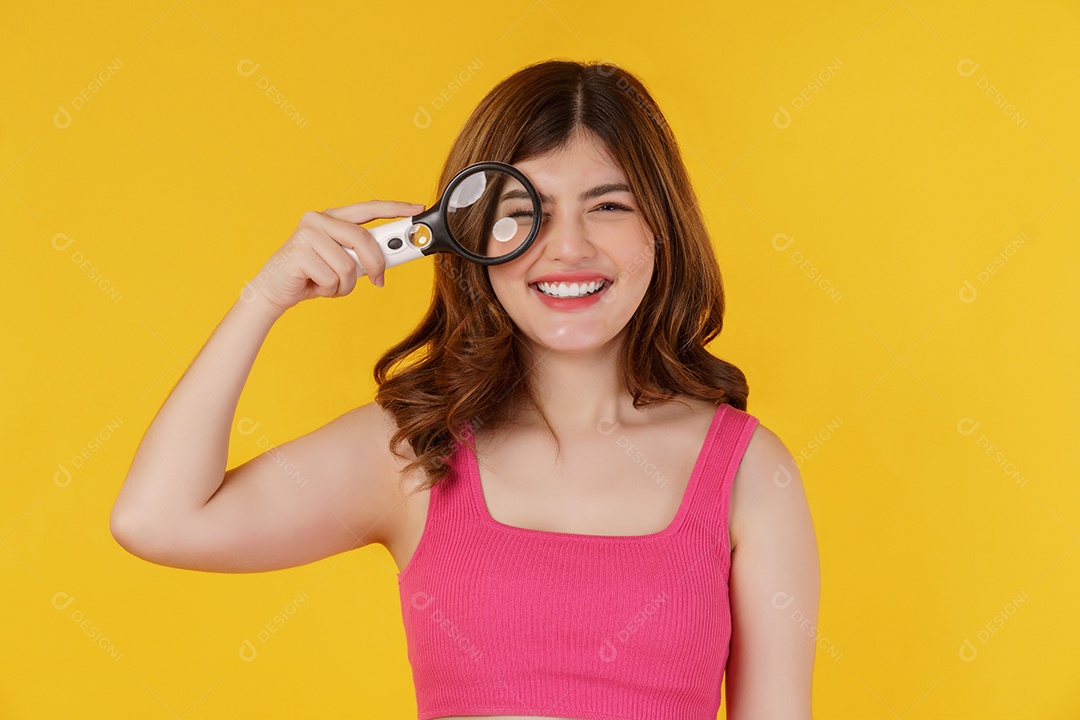 Retrato de mulher bonita detetive alegre olhando para a câmera através de lupa isolada sobre fundo amarelo. Conceito de investigação