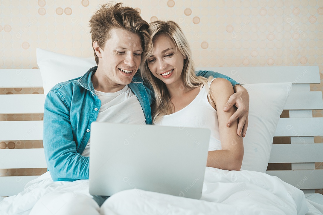 Casal feliz usando o laptop na cama