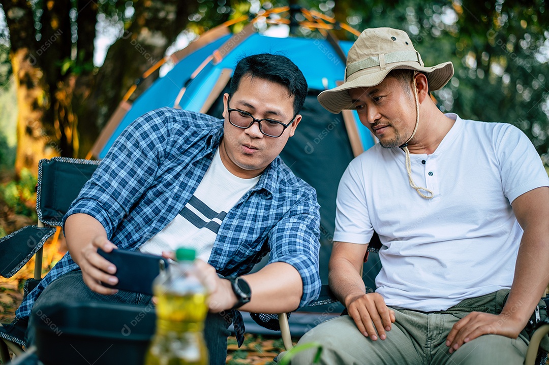 Retrato de homens viajantes asiáticos tirando uma foto no smartphone em um acampamento. Cozinhar ao ar livre, viajar, acampar