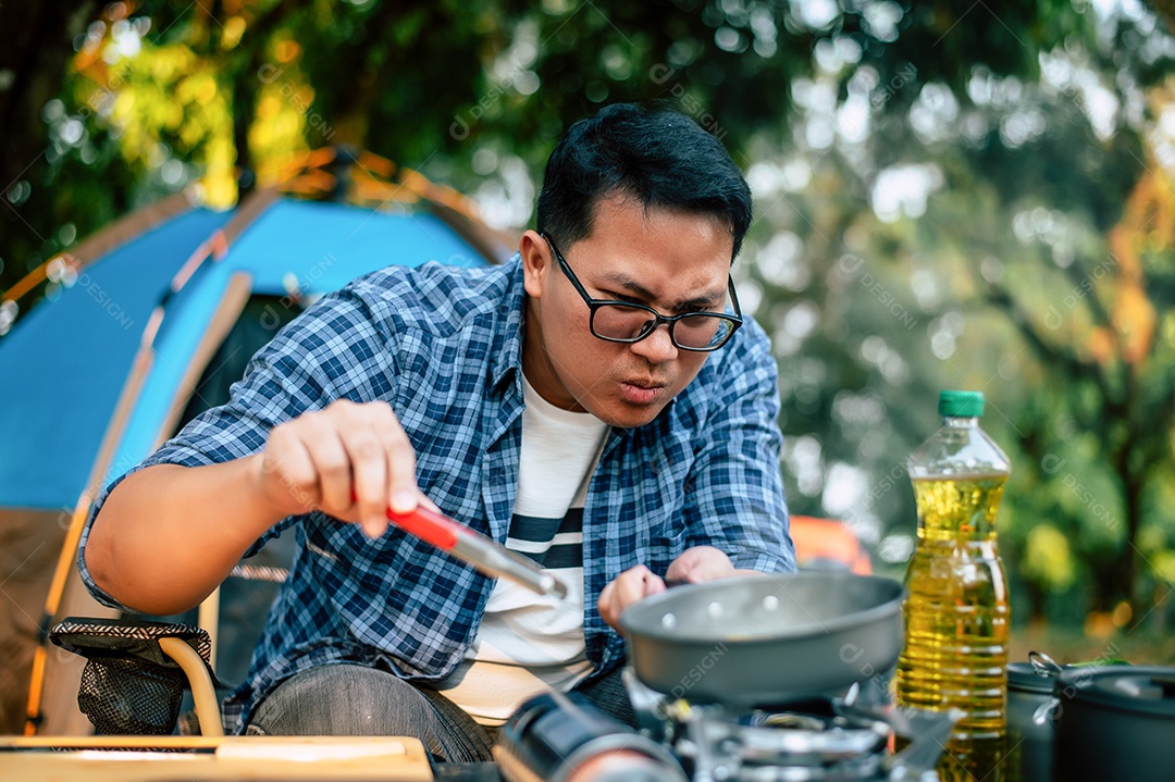 Retrato de óculos de homem viajante asiático fritando um saboroso ovo frito em uma panela quente no acampamento. Cozinhar ao ar livre, viajar, acampar, conceito de estilo de vida.