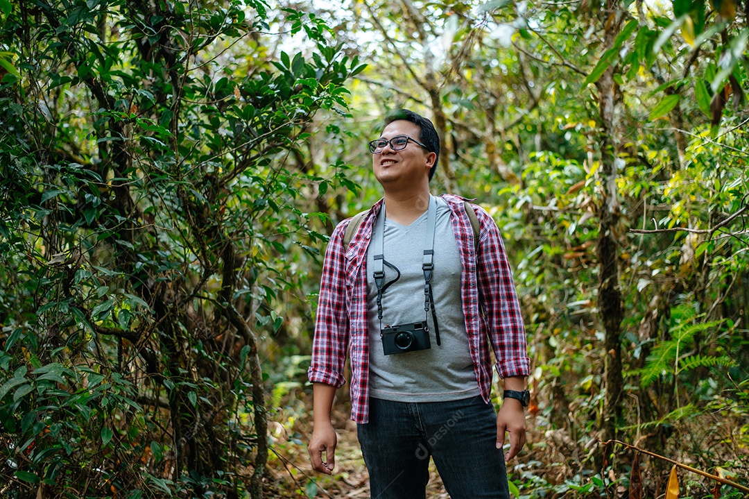 Young asian hiker man with backpack and camera walking on trail in natural forest. copy space