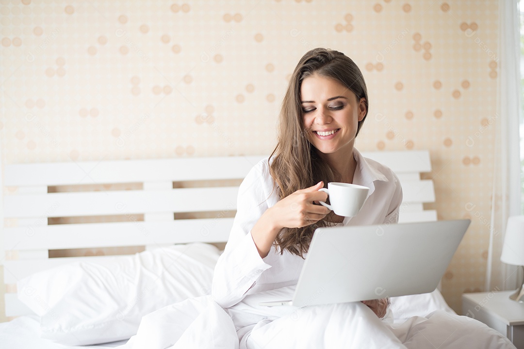 Mulher bonita feliz trabalhando em um laptop na cama em casa