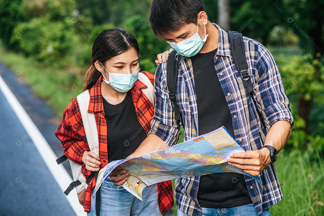 Turistas masculinos e femininos usam máscaras médicas e olham o mapa na rua.