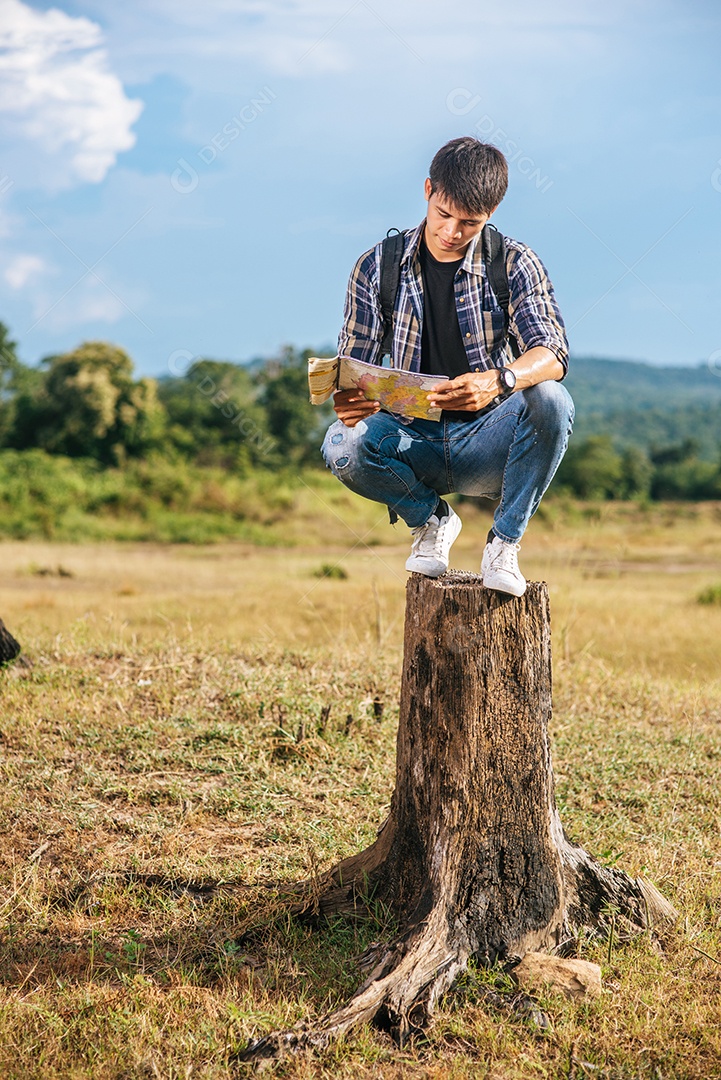 Viajante masculino com uma mochila, carregando um mapa e de pé em um toco de árvore