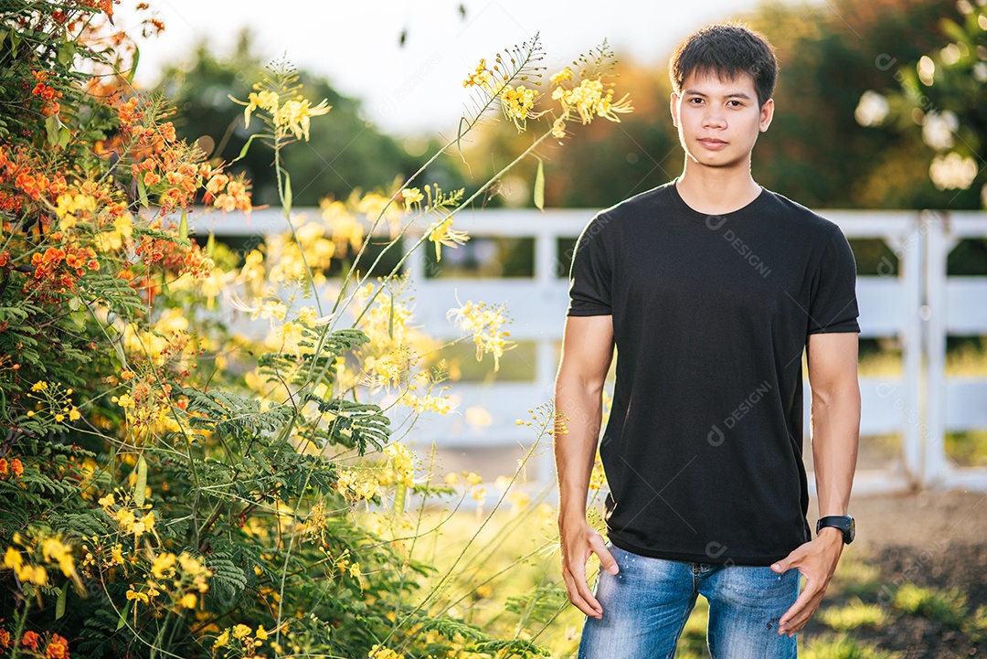 Viajante masculino veste uma camisa preta e fica em um jardim de flores.