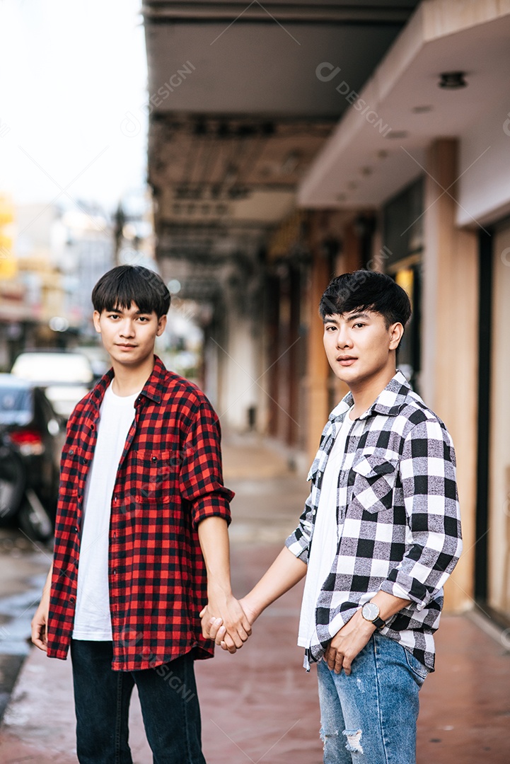 Dois jovens amados em camisas e em pé no meio-fio.