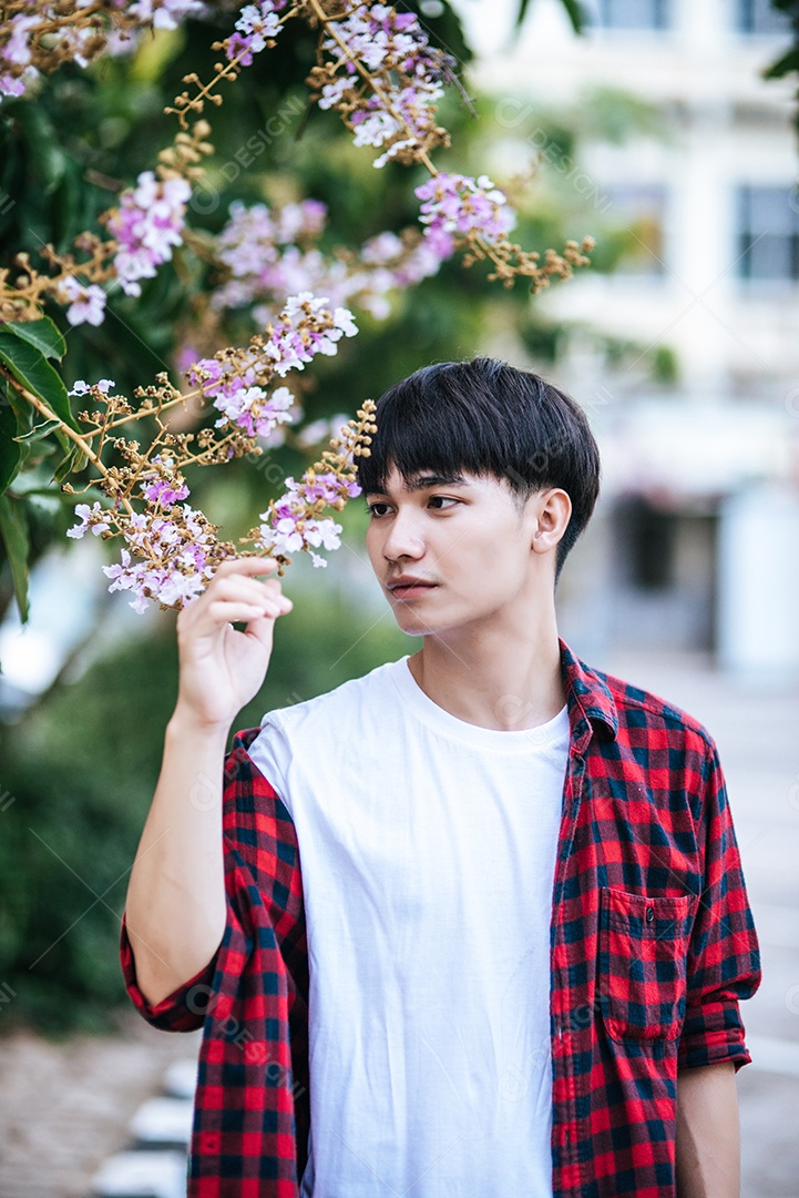 Young man in a striped shirt was standing on the side of the road and holding a flower.