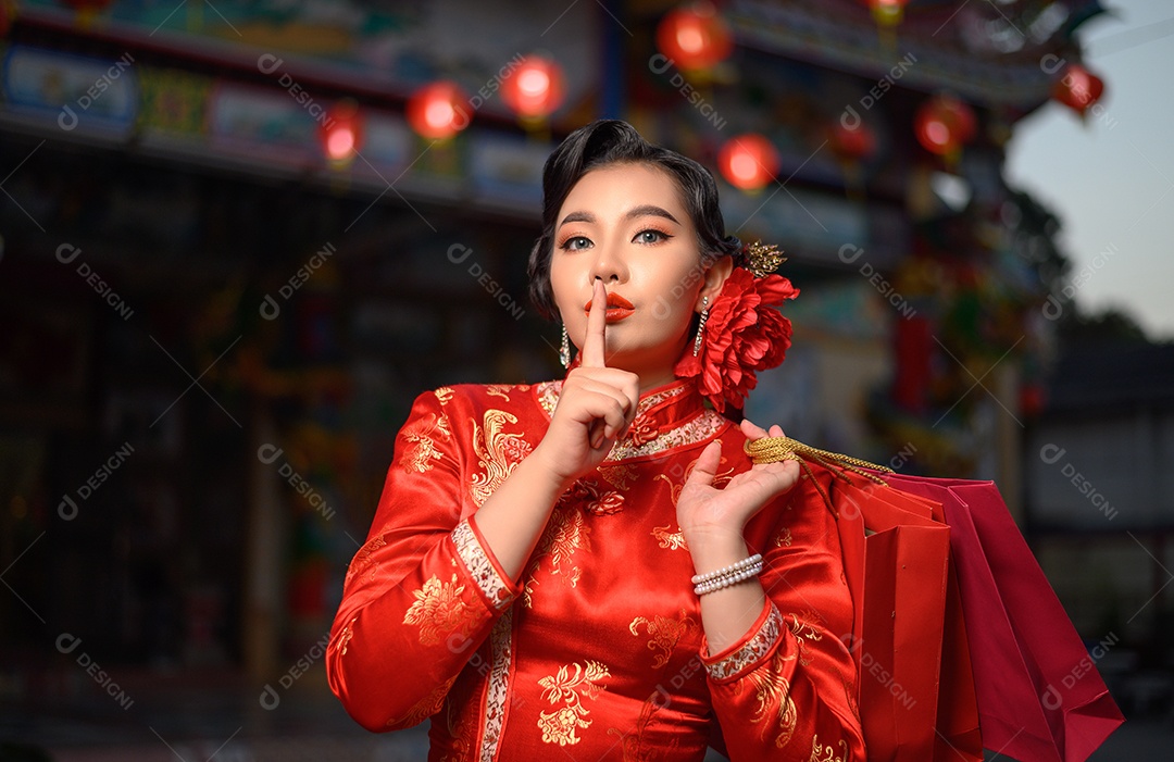 Cena noturna, retrato mulher bonita asiática vestindo um cheongsam sorrindo e coloca o dedo na boca com sacolas de compras no santuário no ano novo chinês, copie o espaço