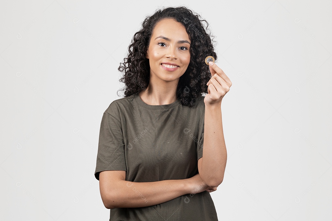 Linda mulher jovem cabelo cacheado sorridente segurando moeda de 1 real cofrinho sobre fundo branco