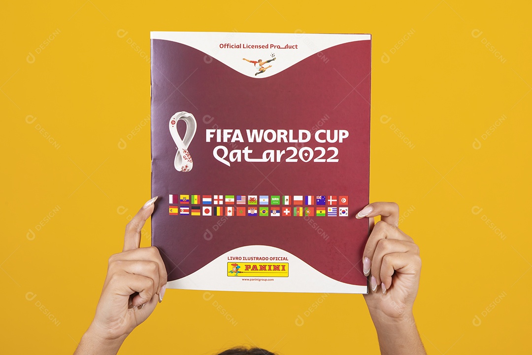 Pessoa segurando álbum da copa do mundo 2022 sobre um fundo isolado amarelo