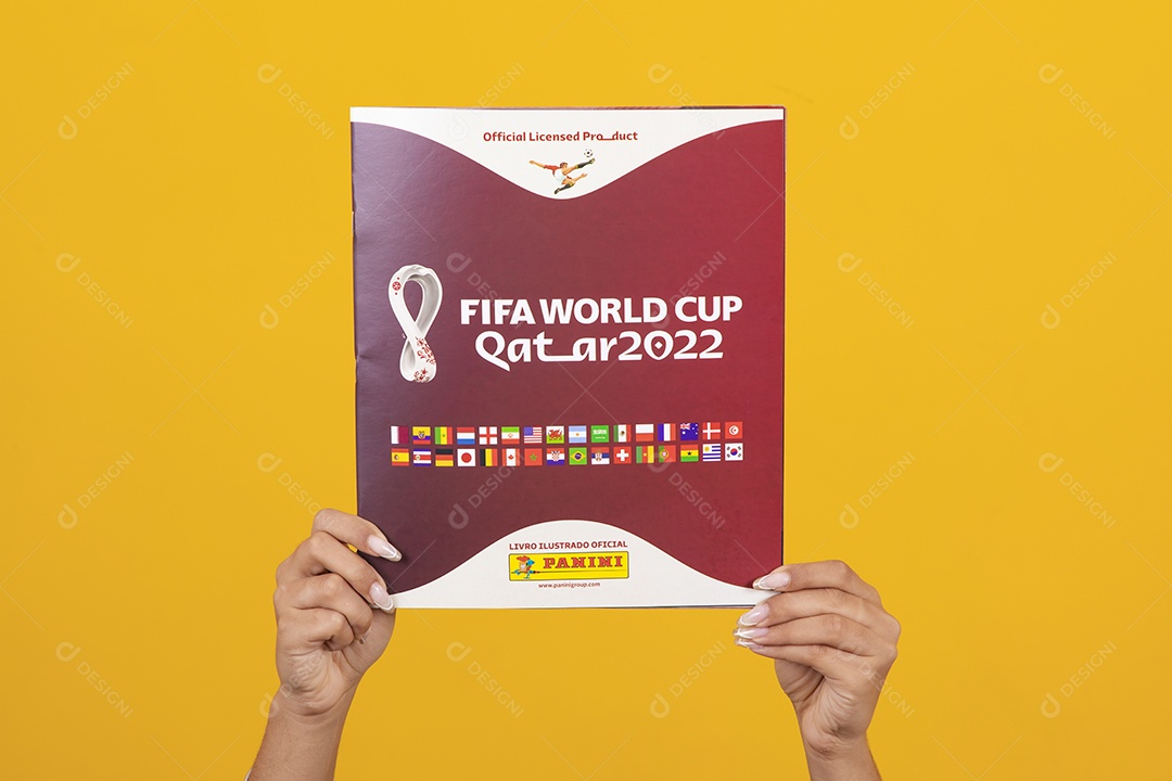 Pessoa segurando álbum da copa do mundo 2022 sobre um fundo isolado amarelo