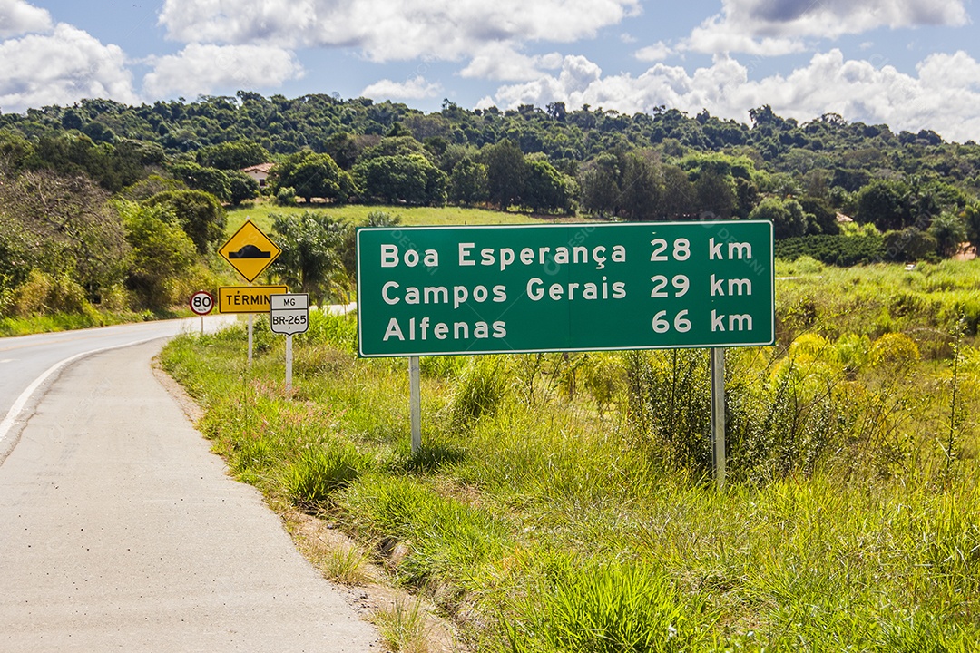 Rodovia com sinalização, placa com informações de cidades próxima com mata ao redor
