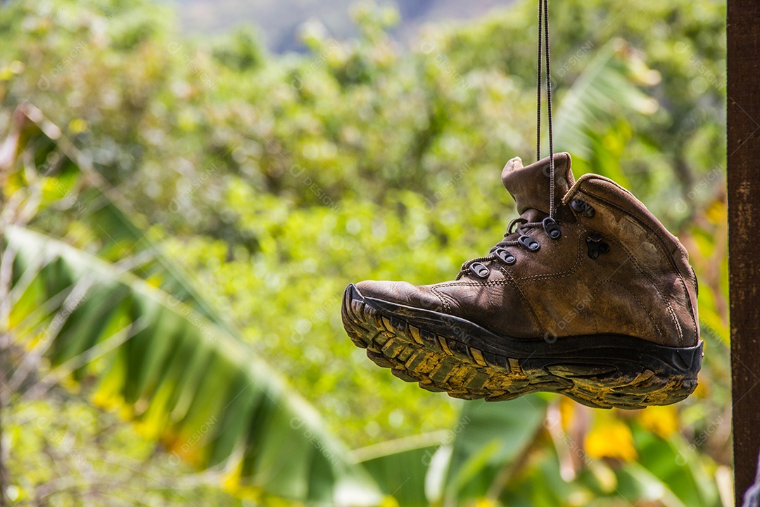 bota de trilha suspensa ao fundo arvores