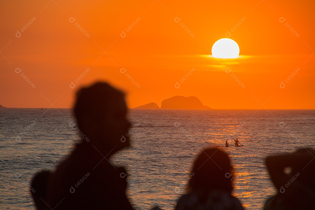 silhueta de pessoas assistindo o pôr do sol na praia do arpoador no rio de janeiro, brasil.