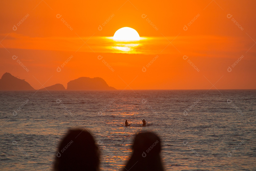silhueta de pessoas assistindo o pôr do sol na praia do arpoador no rio de janeiro, brasil.