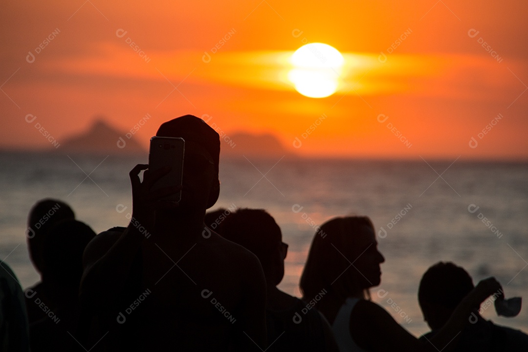 silhueta de pessoas assistindo o pôr do sol na praia do arpoador no rio de janeiro, brasil.