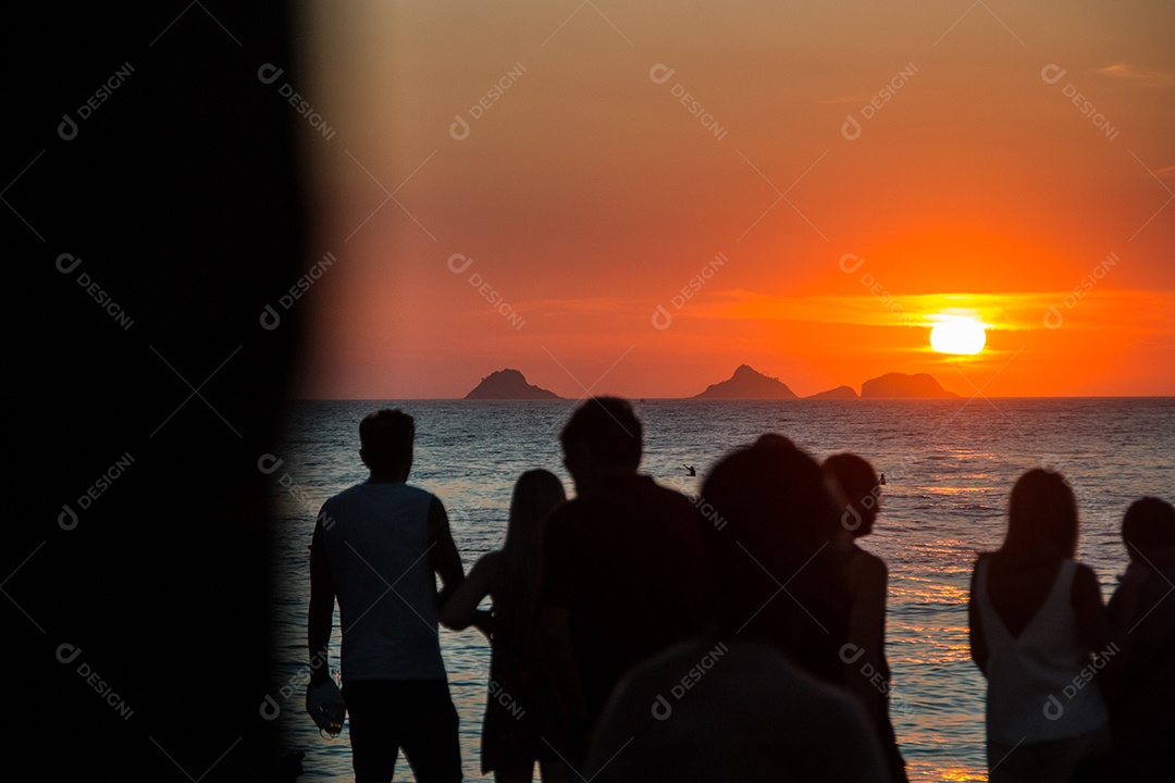 silhueta de pessoas assistindo o pôr do sol na praia do arpoador no rio de janeiro, brasil.