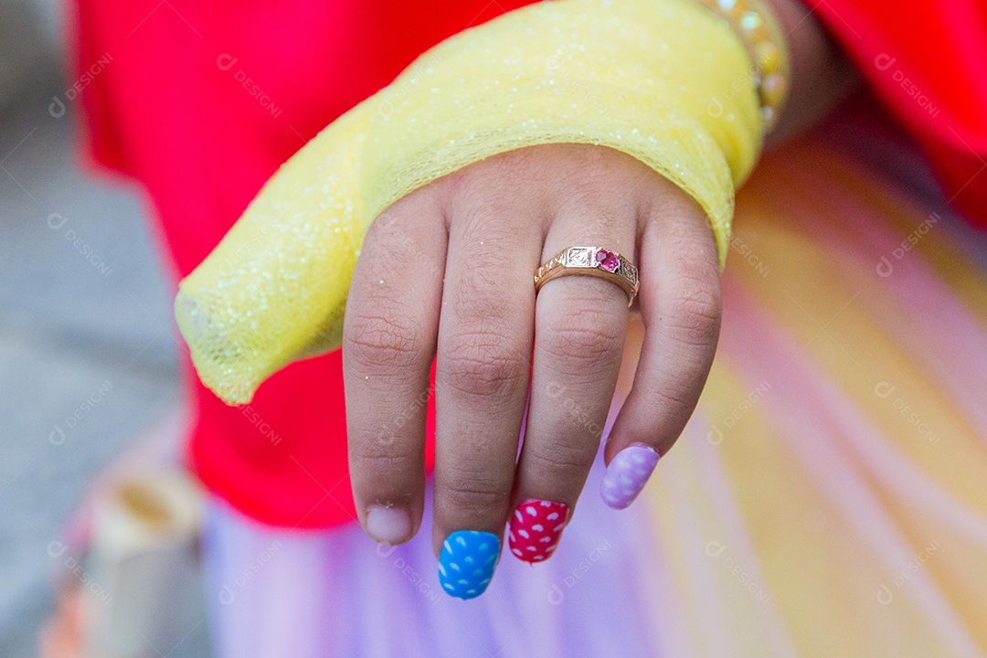 Mão de uma criança com unhas coloridas e anel no dedo no Brasil.
