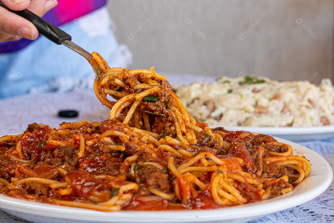 Macarrão espaguete com molho a bolonhesa com acompanhamentos no fundo