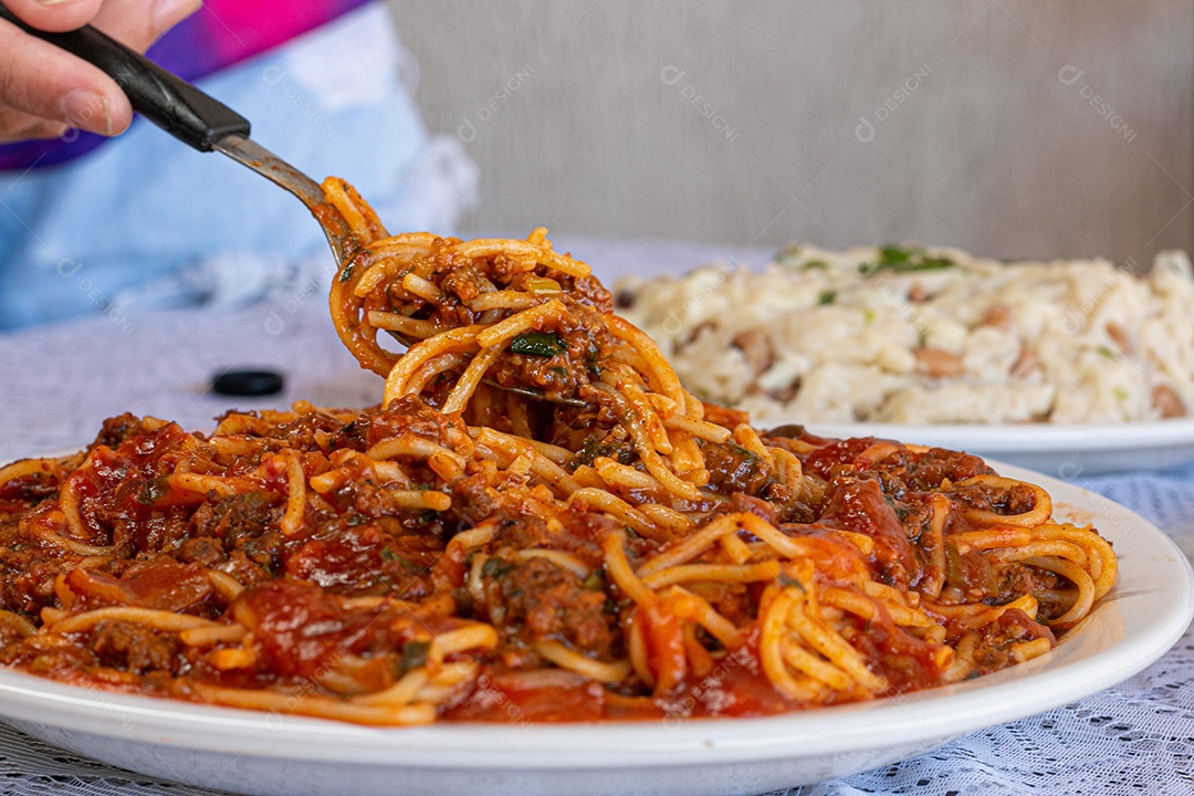 Macarrão espaguete com molho a bolonhesa com acompanhamentos no fundo