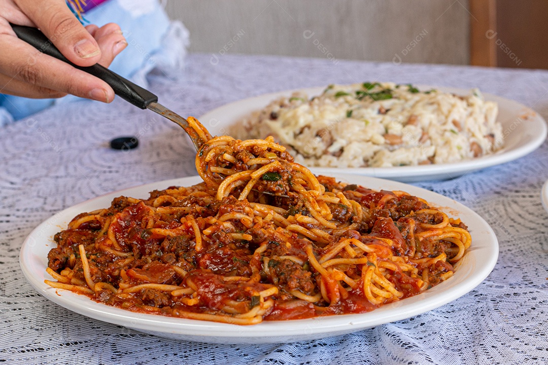 Macarrão espaguete com molho a bolonhesa com acompanhamentos no fundo