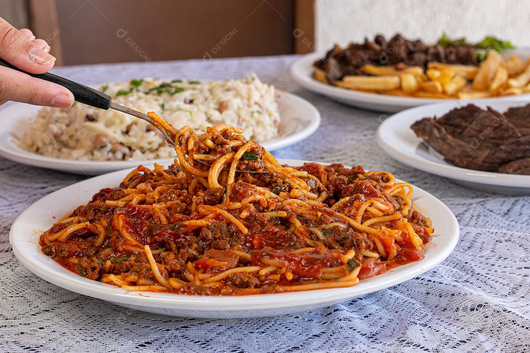 Macarrão espaguete com molho a bolonhesa com acompanhamentos no fundo